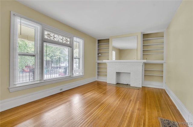 unfurnished living room featuring visible vents, baseboards, built in features, light wood-style floors, and a fireplace