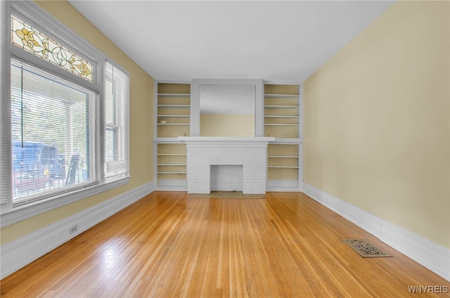 unfurnished living room with built in shelves, a fireplace, visible vents, baseboards, and light wood-type flooring