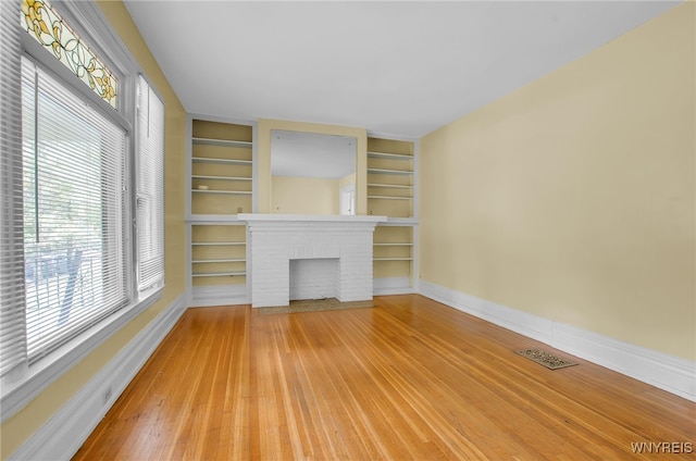 unfurnished living room with built in features, a fireplace, visible vents, light wood-type flooring, and baseboards