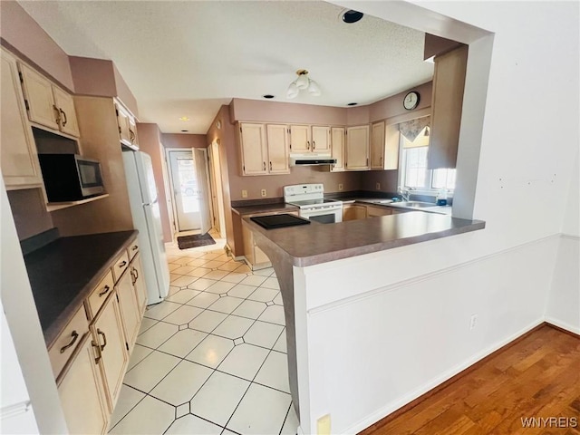 kitchen featuring under cabinet range hood, a peninsula, white appliances, a sink, and baseboards