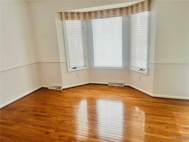 unfurnished room featuring baseboards, visible vents, and hardwood / wood-style floors