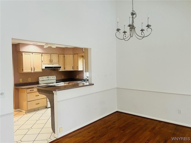 kitchen with white electric stove, dark countertops, an inviting chandelier, under cabinet range hood, and a sink