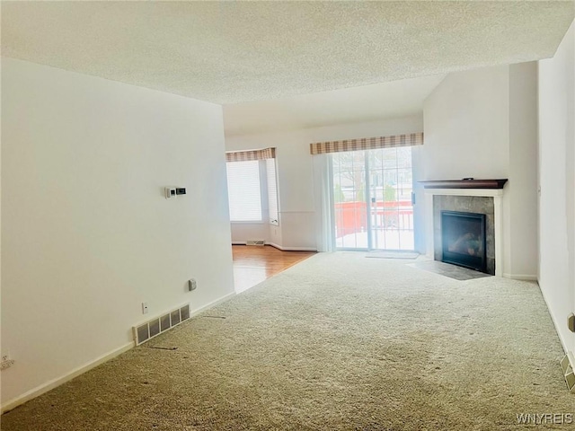 unfurnished living room with carpet floors, visible vents, a fireplace, and a textured ceiling