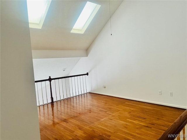 additional living space with vaulted ceiling with skylight, wood finished floors, and baseboards