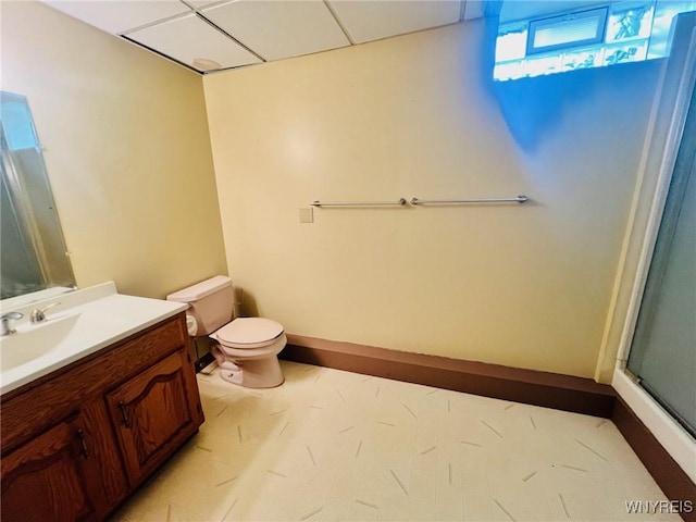 bathroom with a paneled ceiling, toilet, a shower with shower door, vanity, and baseboards