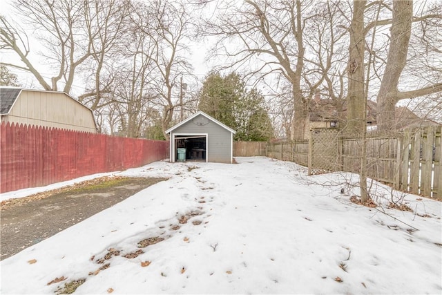 snowy yard with a garage, an outbuilding, and a fenced backyard