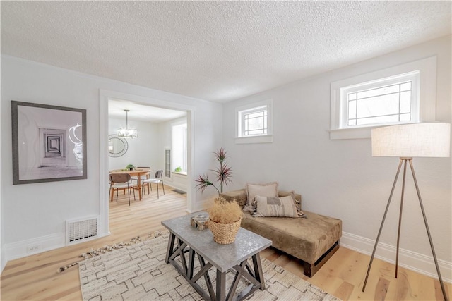 living room with visible vents, a textured ceiling, an inviting chandelier, and wood finished floors