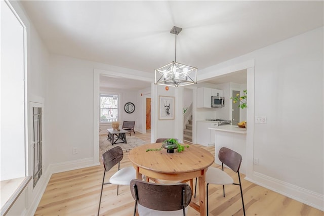 dining room featuring a notable chandelier, stairway, baseboards, and light wood-style floors