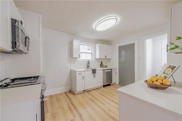 kitchen with white cabinets, light wood-style flooring, appliances with stainless steel finishes, backsplash, and a sink