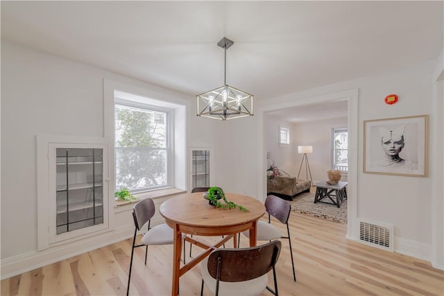 dining space featuring baseboards, light wood-type flooring, visible vents, and an inviting chandelier