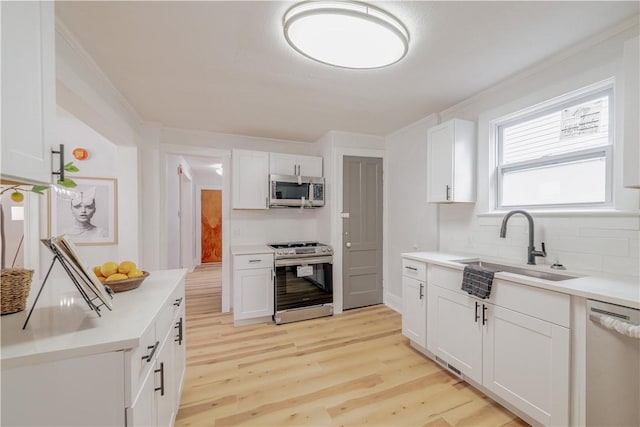 kitchen featuring light wood-style flooring, a sink, white cabinets, appliances with stainless steel finishes, and tasteful backsplash