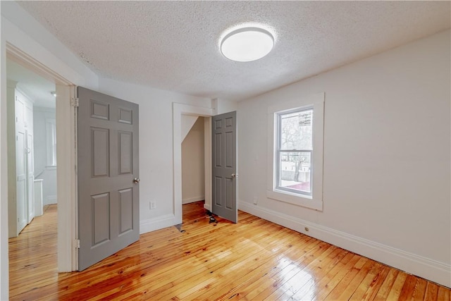 unfurnished bedroom featuring baseboards, a textured ceiling, and light wood-style floors