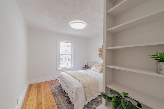 bedroom with light wood-style floors, a textured ceiling, and baseboards