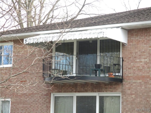 view of side of property with roof with shingles, brick siding, and a balcony