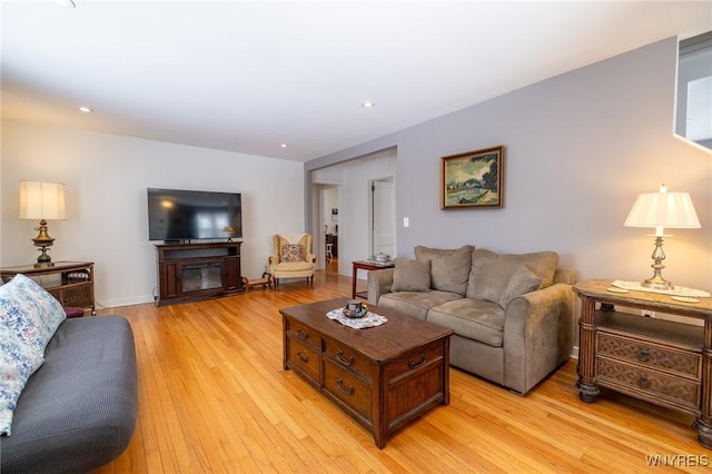 living room featuring recessed lighting, light wood-style flooring, and a glass covered fireplace