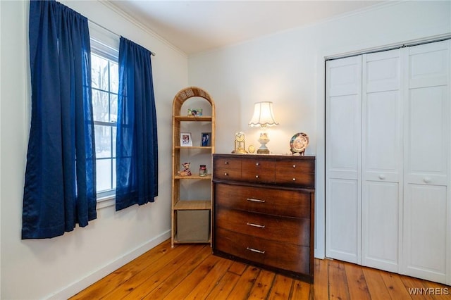 bedroom with hardwood / wood-style flooring, crown molding, baseboards, and a closet