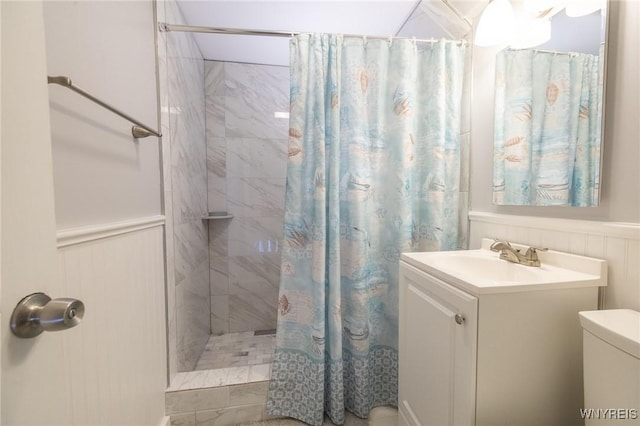 full bathroom featuring wainscoting, vanity, toilet, and tiled shower