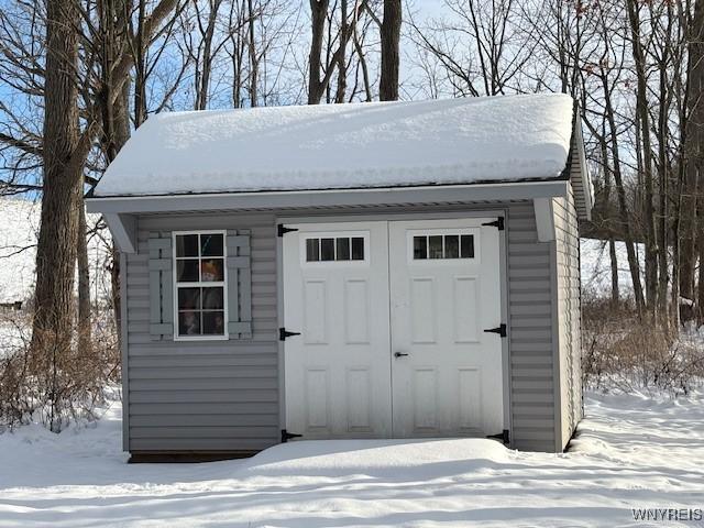 snow covered structure featuring a storage unit and an outdoor structure