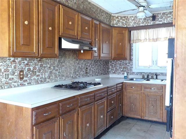 kitchen featuring under cabinet range hood, stainless steel gas cooktop, a sink, a ceiling fan, and light countertops