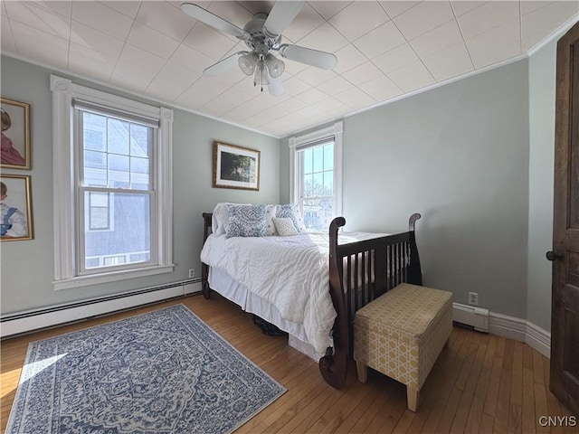 bedroom featuring baseboards, wood-type flooring, ceiling fan, ornamental molding, and a baseboard heating unit