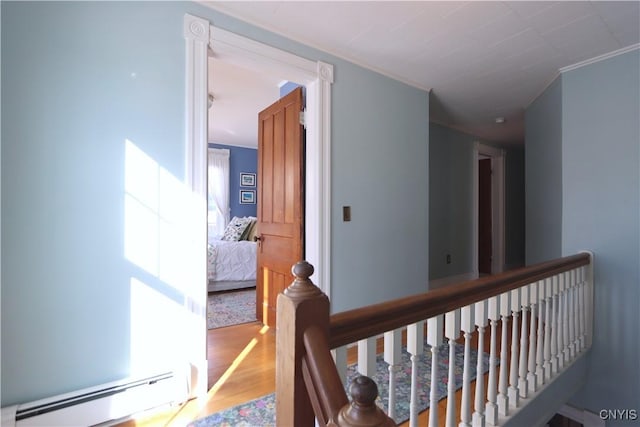 corridor with ornamental molding, a baseboard radiator, wood finished floors, and an upstairs landing