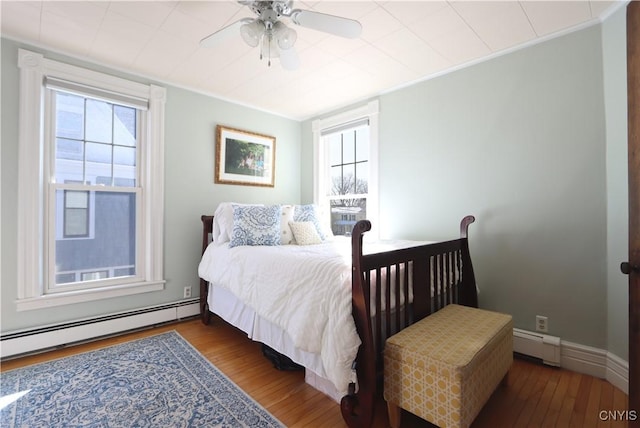 bedroom with baseboard heating, a baseboard radiator, wood finished floors, and crown molding