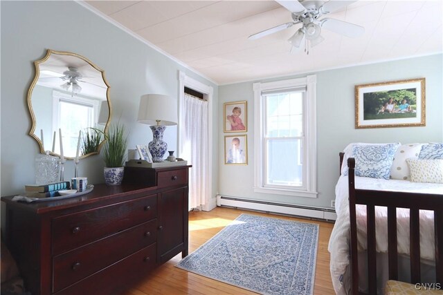 bedroom featuring crown molding, light wood finished floors, baseboard heating, and ceiling fan