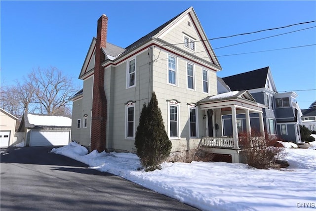 view of front of property featuring a garage, a chimney, a porch, and an outbuilding