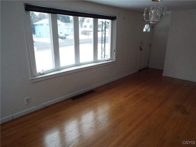 empty room featuring visible vents, a notable chandelier, baseboards, and wood finished floors