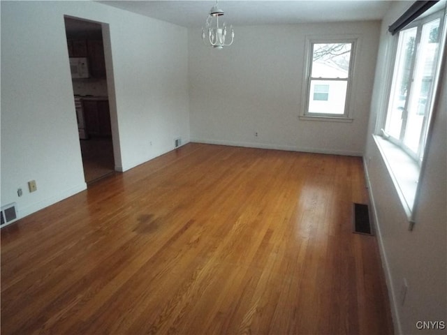 unfurnished dining area with baseboards, wood finished floors, visible vents, and an inviting chandelier