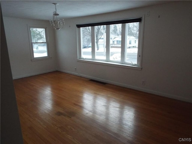 empty room featuring a notable chandelier, baseboards, visible vents, and wood finished floors