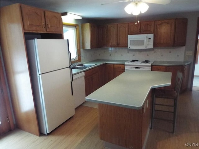 kitchen featuring light countertops, light wood-style flooring, backsplash, a sink, and white appliances