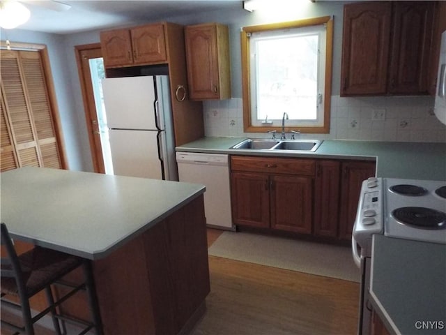 kitchen featuring a breakfast bar area, light countertops, backsplash, a sink, and white appliances