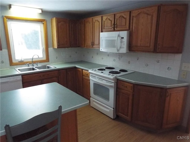 kitchen featuring backsplash, brown cabinetry, a sink, light wood-type flooring, and white appliances