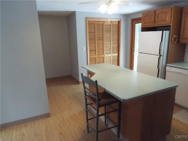 kitchen with white appliances, baseboards, a kitchen island, a kitchen breakfast bar, and light wood-type flooring