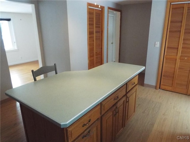 kitchen featuring light wood-style flooring, baseboards, light countertops, a center island, and brown cabinetry