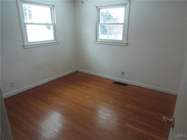 unfurnished room featuring baseboards, visible vents, and wood finished floors