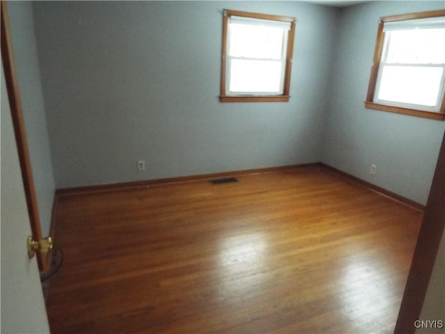 spare room with wood finished floors, visible vents, and baseboards