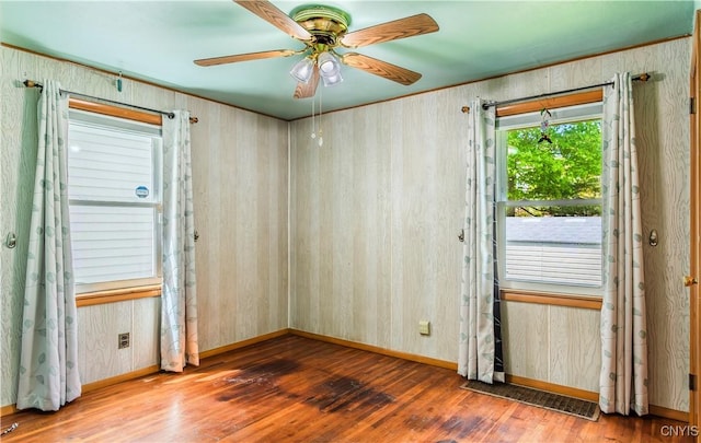 empty room with ceiling fan, wood walls, wood-type flooring, and baseboards