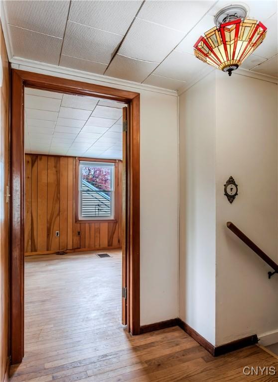 hallway with hardwood / wood-style flooring, baseboards, visible vents, and wood walls