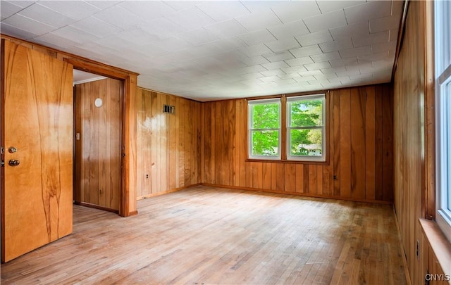 unfurnished room featuring light wood-type flooring, wood walls, baseboards, and visible vents