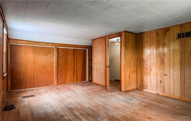 unfurnished bedroom featuring light wood-type flooring, wood walls, baseboards, and visible vents