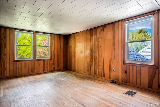 spare room featuring wood walls, baseboards, visible vents, and hardwood / wood-style floors