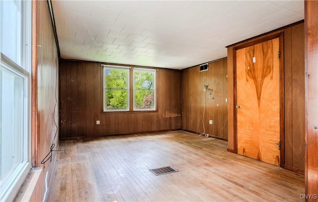 empty room featuring light wood finished floors, visible vents, and wood walls