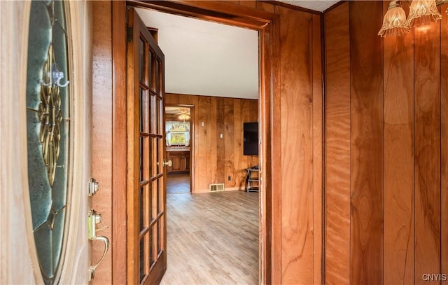 hall with wood walls, wood finished floors, visible vents, and baseboards