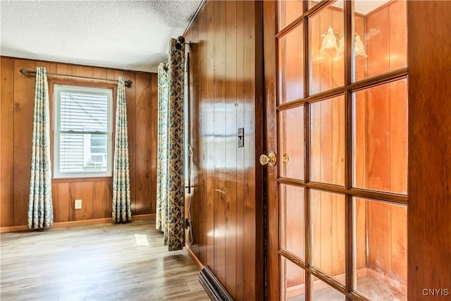 doorway with a textured ceiling, baseboards, wood finished floors, and wooden walls