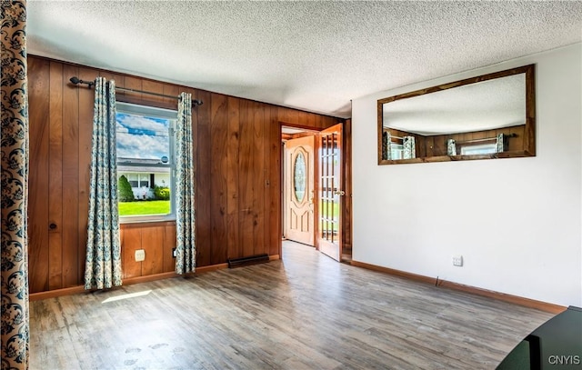 unfurnished room with wooden walls, a textured ceiling, baseboards, and wood finished floors