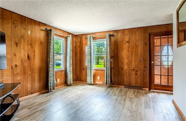 spare room featuring wooden walls, baseboards, visible vents, wood finished floors, and a textured ceiling