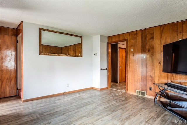 unfurnished living room featuring visible vents, wooden walls, baseboards, and wood finished floors