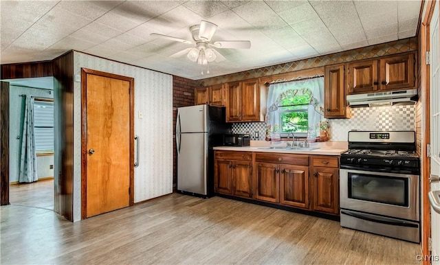 kitchen with under cabinet range hood, stainless steel appliances, a sink, and brown cabinetry